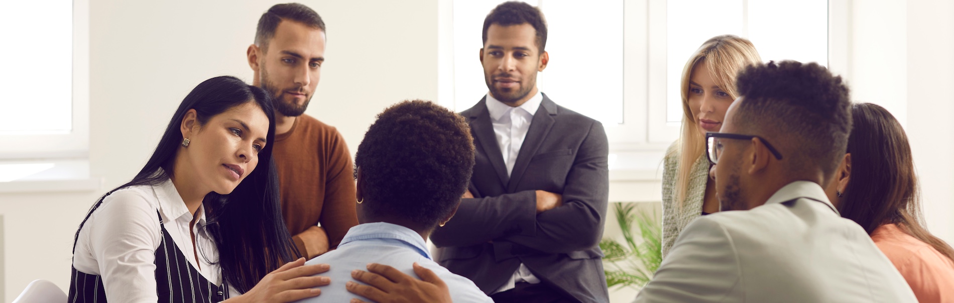 A diverse group of people sitting in a circle during a group therapy session for drug rehabilitation with a counselor and participants in a bright, modern room.