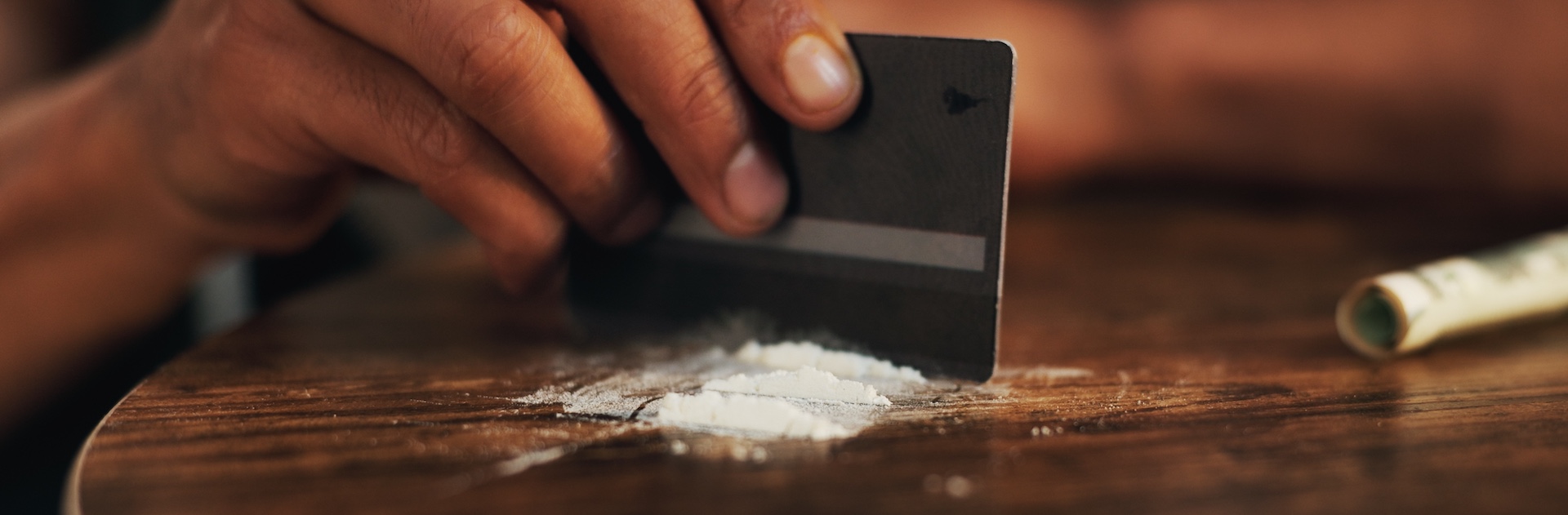 A person's hands are using a black credit card to arrange white powder lines on a wooden surface, representing refusing addiction treatment and continued substance abuse.